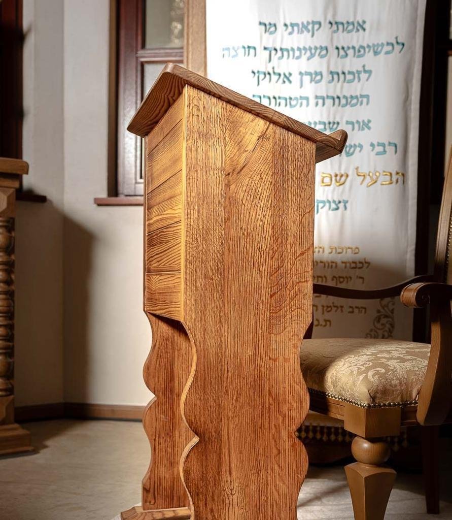 Restored wooden shtender lectern and bench beneath a portrait of the Baal Shem Tov